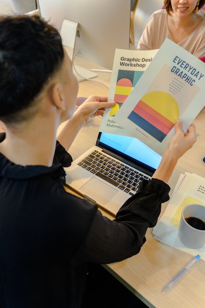 services-03 A professional reviews colorful graphic design brochures at a laptop in a modern office environment.