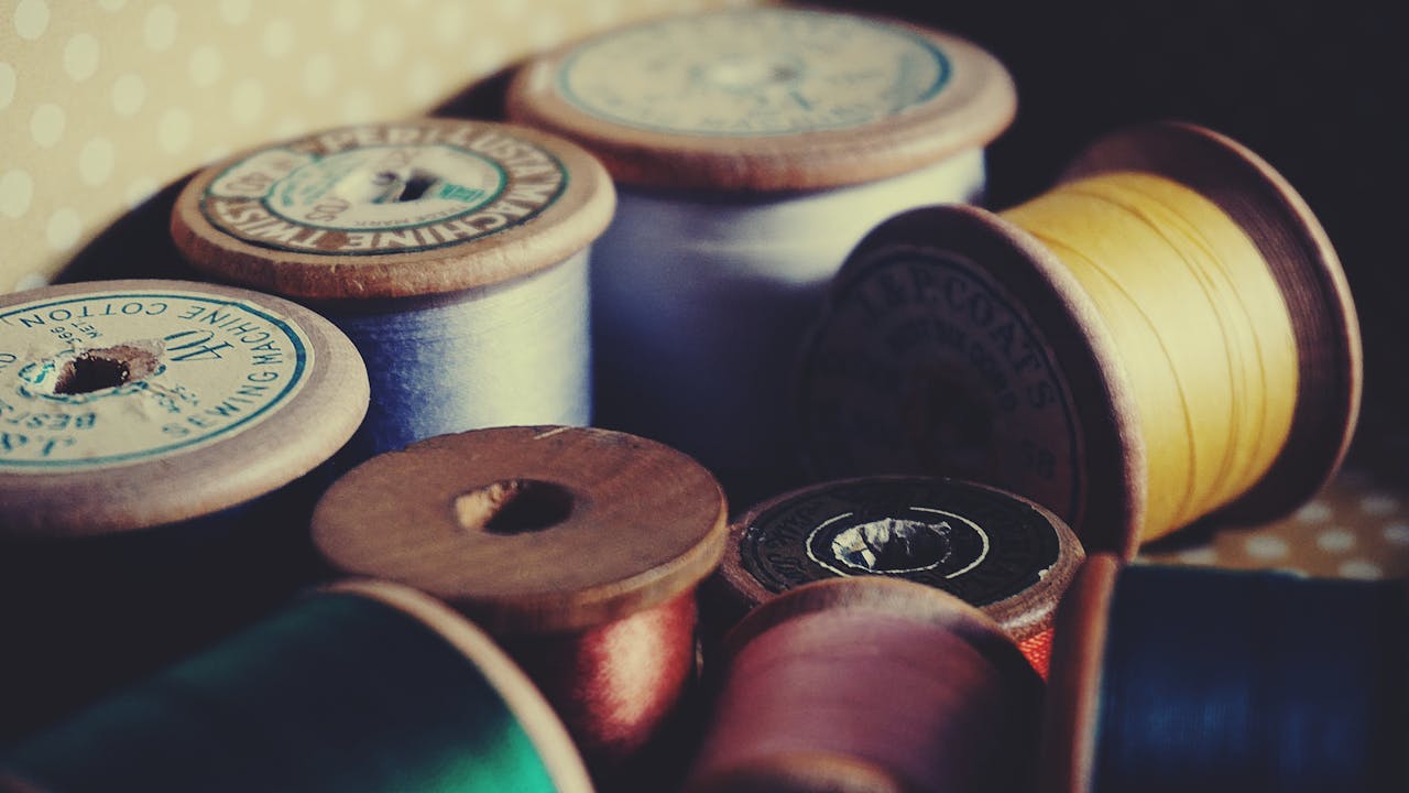 contact-img-02 A close-up of vintage wooden spools displaying colorful sewing threads for crafting and tailoring.