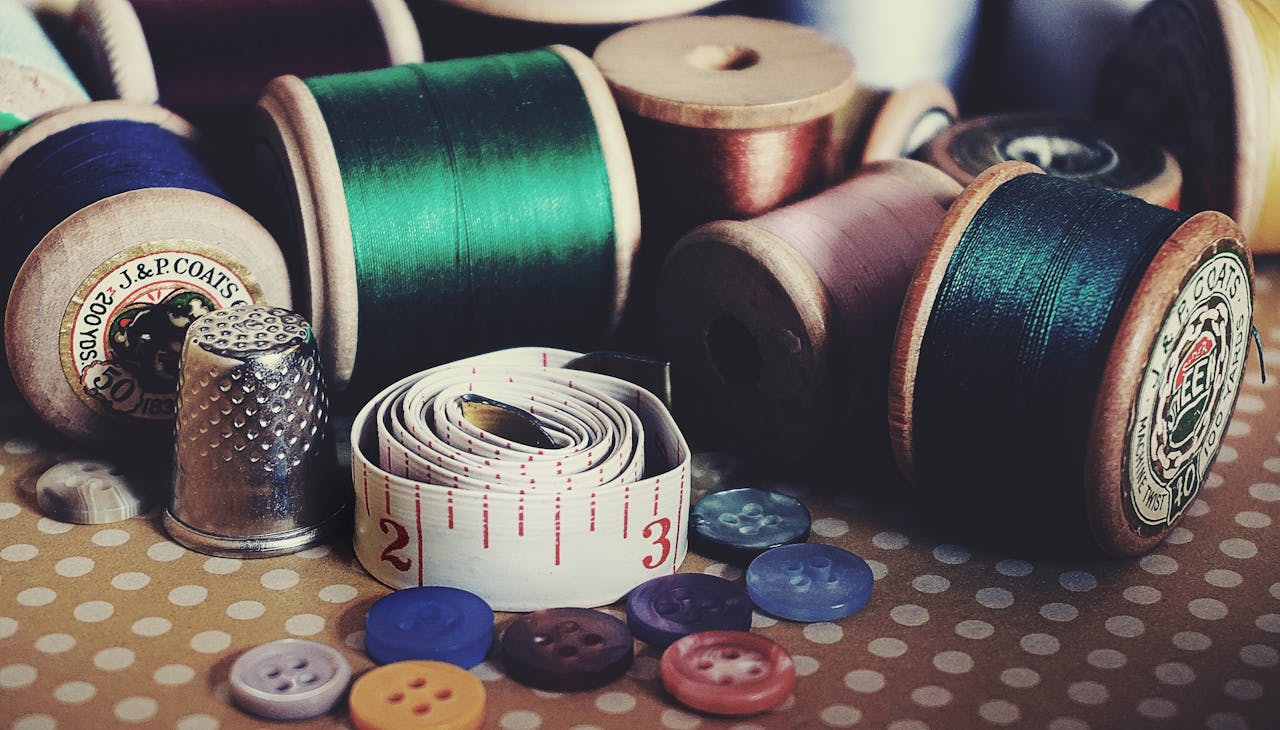 services-03 Close-up of vintage sewing essentials including threads, buttons, thimble, and measuring tape.