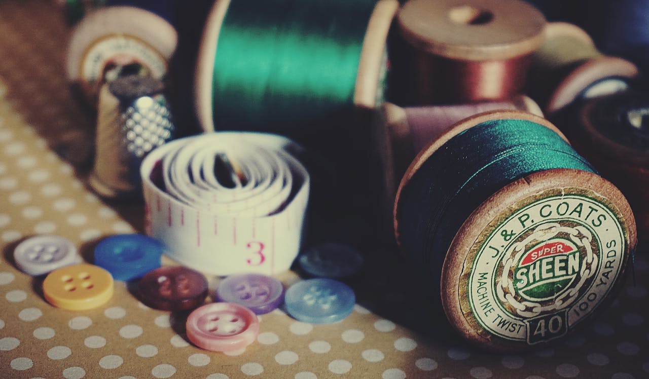 contact-img-01 A collection of vintage sewing supplies including spools, buttons, and a tape measure on a polka dot tablecloth.