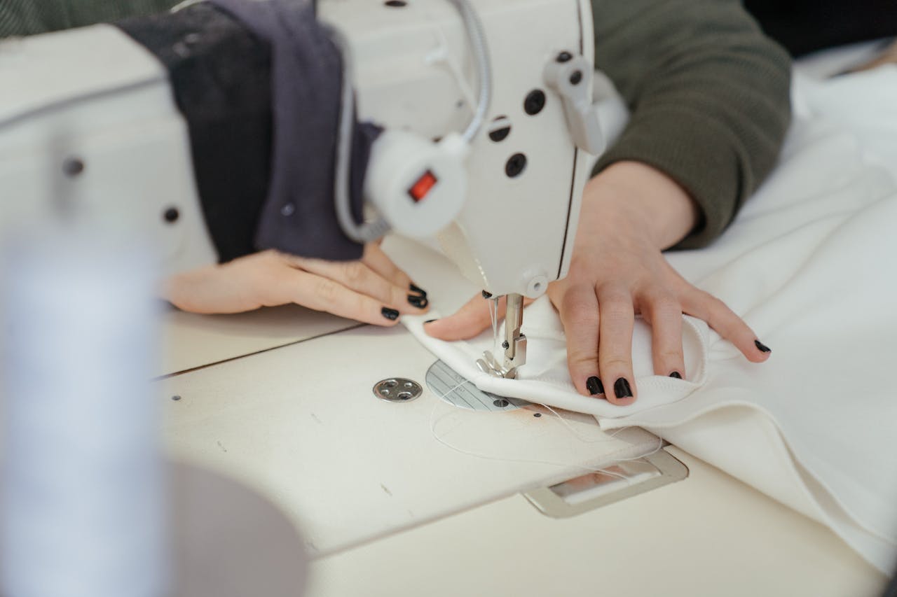 about-img-01 Close-up of hands sewing fabric on a professional sewing machine in a workshop.