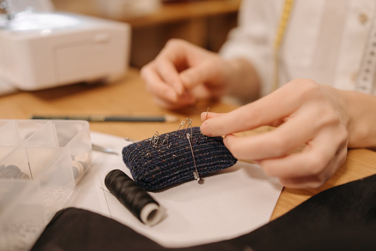 services-img-02 Hands working on sewing fabric with pins and needles, close-up view.