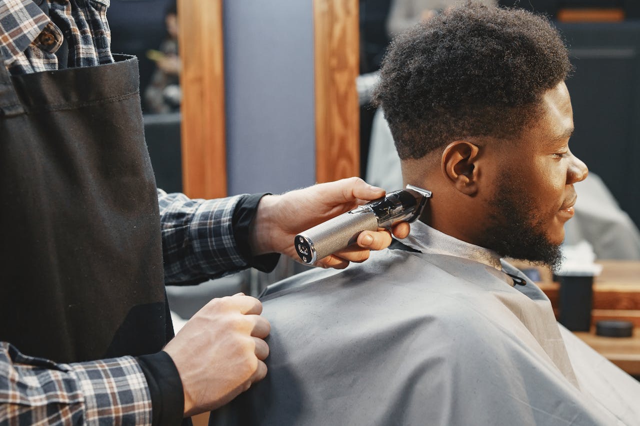 A barber trims an adult man's hair using clippers in a contemporary salon setting.